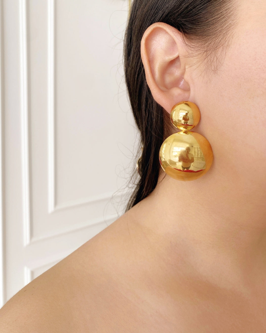 Aretes de circulos dobles dorados grandes puestos en oreja femenina.