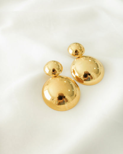 Aretes de circulos dobles dorados minimalistas sobre fondo de tela blanca.