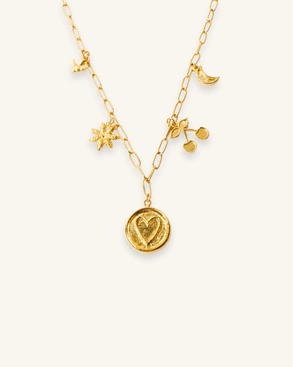 Primer plano de la Cadena Multicharms, resaltando sus dijes de corazón, cereza, luna, flor y ave en bronce con baño en oro de 24K.