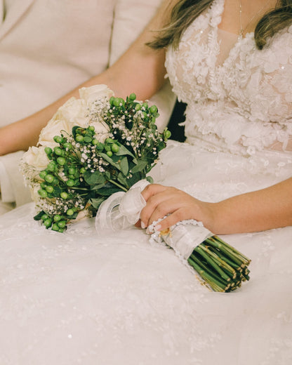 Novia sosteniendo su ramo decorado con una camandula de novia dorada, un símbolo de fe y bendición en el matrimonio.