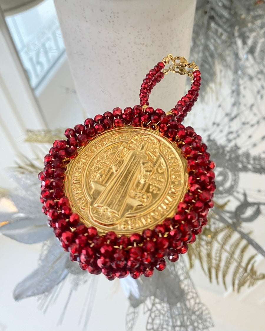 Medalla de San Benito dorada con cristales rojos y broche dorado.